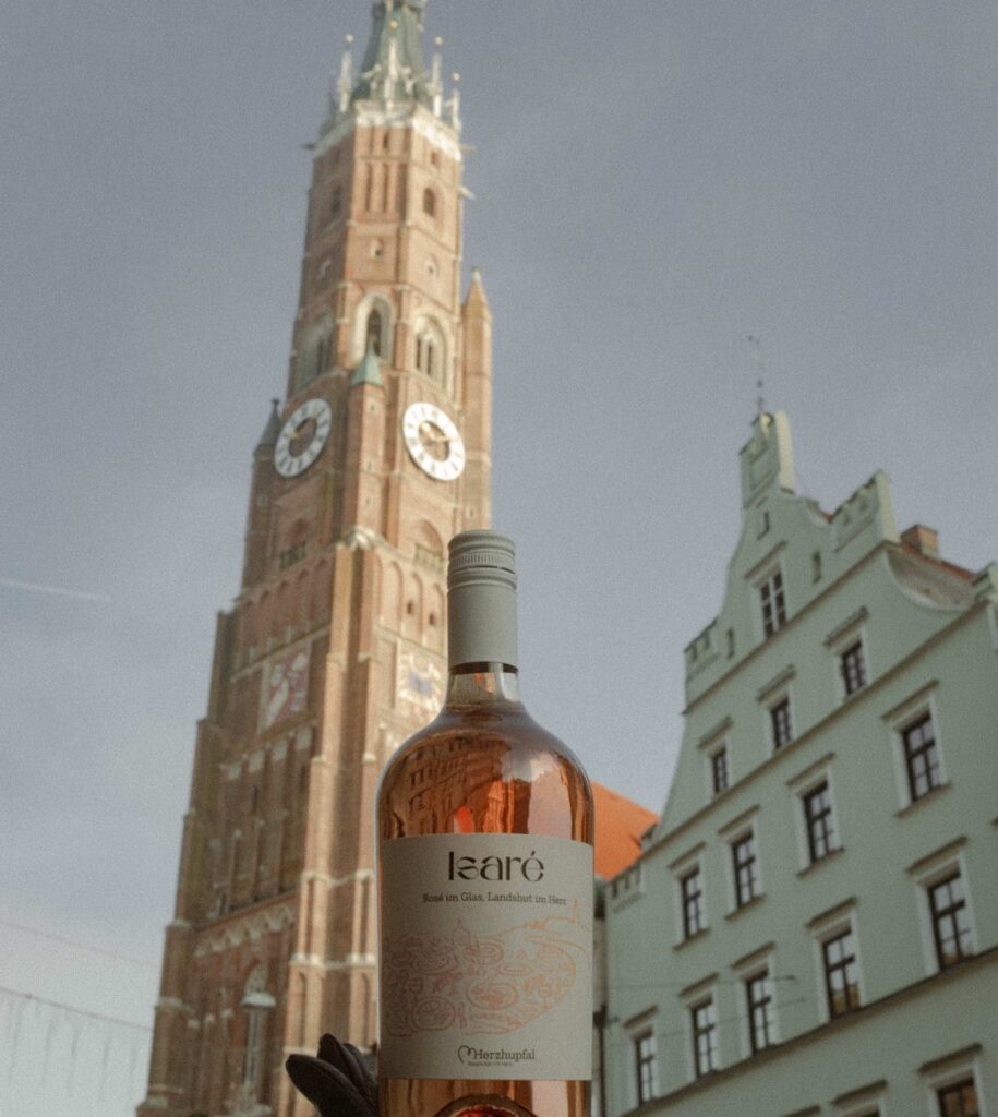 Eine Hand hält die Isaré-Flasche vor den Turm der Martinskirche in Landshut